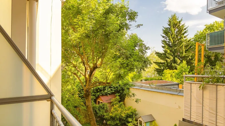 Blick vom Balkon auf einen grünen Hinterhof mit Spielhaus und Bäumen.