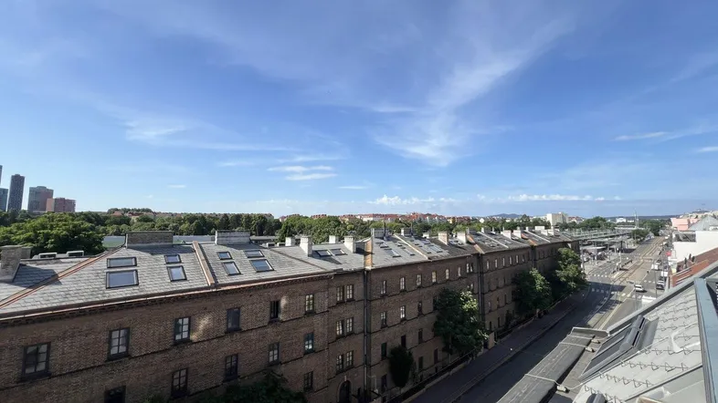 Weitläufiger Blick über die Dächer der Stadt mit angrenzender Straße und Gebäuden unter blauem Himmel.