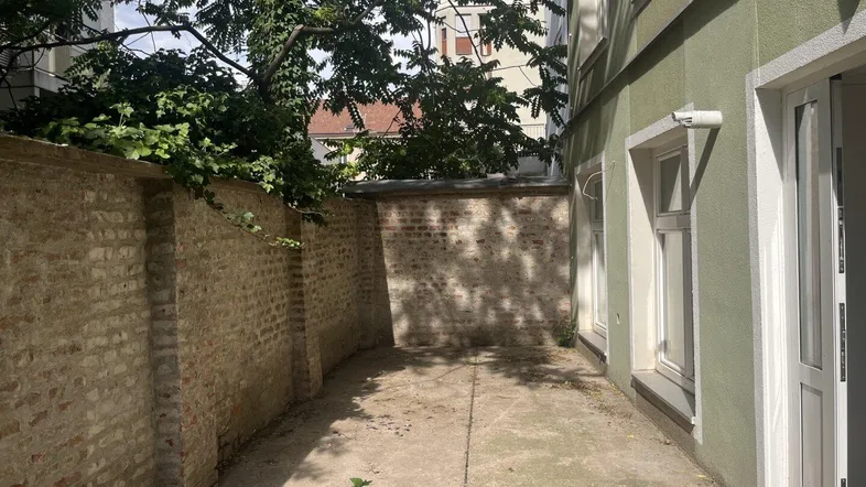 Eine gepflasterte Außenfläche neben einem Gebäude mit einer Ziegelmauer und Bäumen im Hintergrund.
