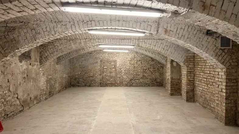 Geräumiger Gewölbekeller mit unverputzten Ziegelwänden und Betonboden, beleuchtet von Leuchtstoffröhren.