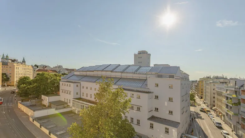 Weitläufige Ansicht eines Gebäudes mit Solaranlagen auf dem Dach und umliegender Stadtlandschaft.