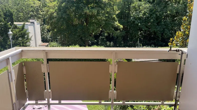 Balkon mit Sichtschutz und Blick auf üppige grüne Bäume unter blauem Himmel.