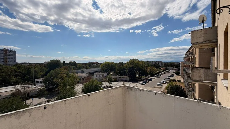 Weitblick vom Balkon über die Stadt mit Bäumen und umliegenden Gebäuden unter blauem Himmel.