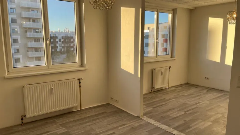 Helles Zimmer mit zwei Fenstern, strukturiertem Deckenmuster und Blick auf umliegende Gebäude.