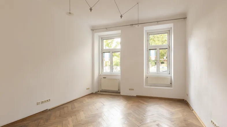 Helles Zimmer mit Fischgrätparkettboden und zwei Fenstern, bereit zur individuellen Gestaltung.