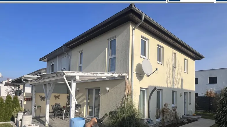 Geräumige Terrasse mit Pergola und Gartenbereich hinter dem Haus unter blauem Himmel.