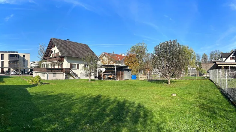 Große Rasenfläche mit einem Einfamilienhaus im Hintergrund unter blauem Himmel.