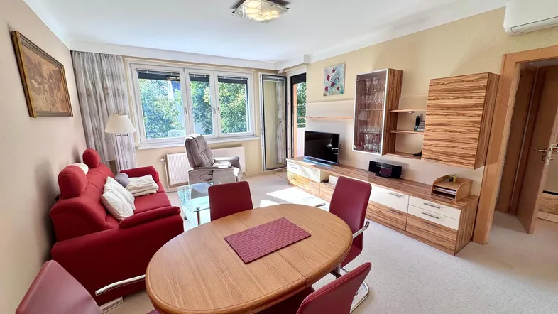 Heller Wohn- und Essbereich mit rotem Sofa, Holztisch und Zugang zum Balkon.