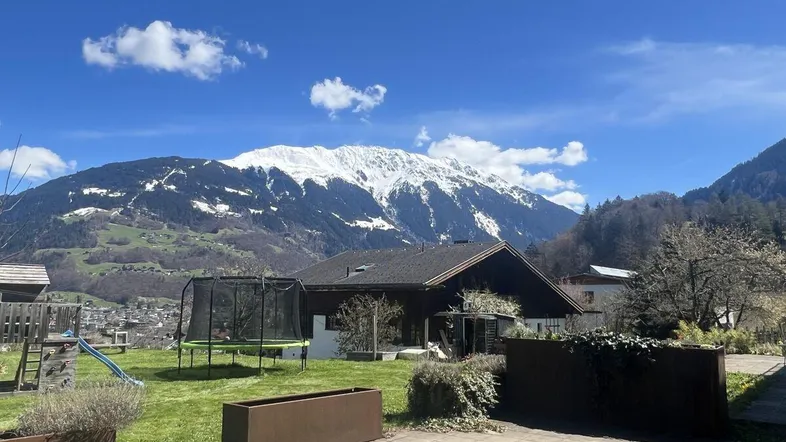Großzügiger Gartenbereich mit Trampolin und Spielplatz, umgeben von einer beeindruckenden Bergkulisse.