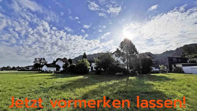 Sonnige Landschaft mit grünen Feldern, Häusern im Hintergrund und Bergen am Horizont.