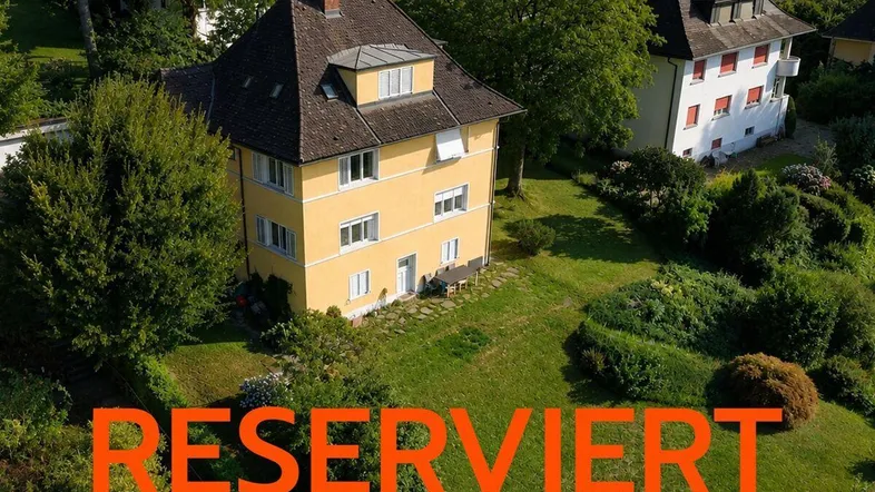 Luftaufnahme eines gelben Hauses mit großem Garten und umliegender Grünfläche.