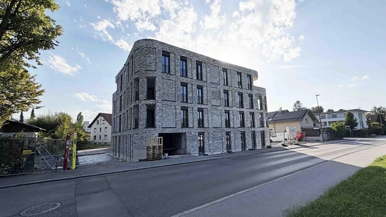 Modernes Neubaugebäude mit markanter grauer Ziegelfassade und großen Fenstern an einer Straßenecke.
