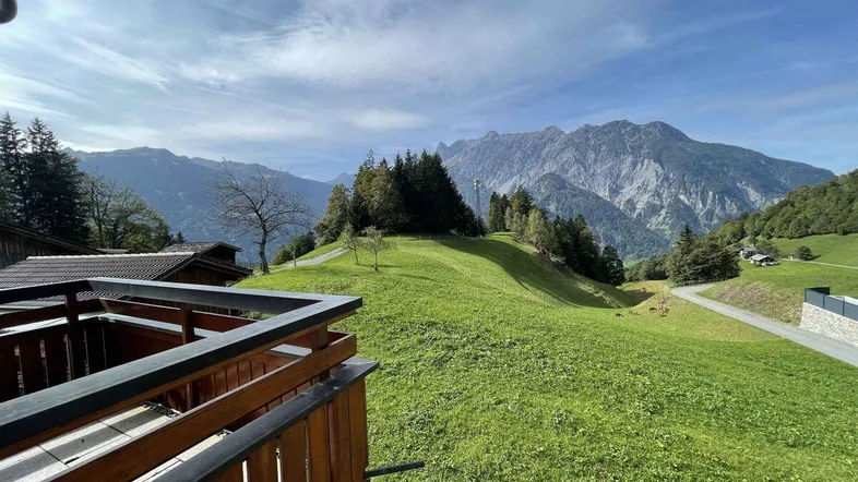 Panoramablick vom Balkon auf die majestätischen Berge und grüne Hügellandschaft unter blauem Himmel.