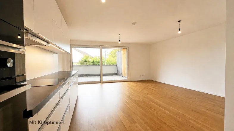 Heller offener Wohnbereich mit integrierter Küche, Holzboden und Zugang zu einem Balkon.