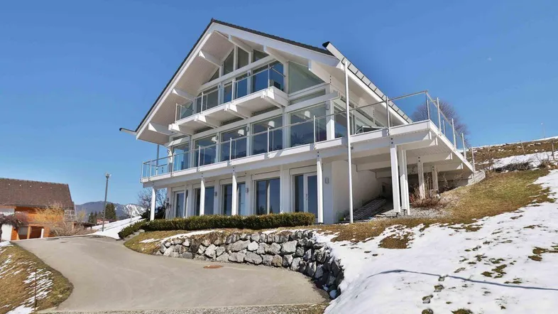 Modernes Haus mit großen Glasflächen und Balkonen, umgeben von Schnee und einer Auffahrt.