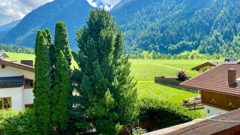 Blick von einem Balkon auf die umliegende Berglandschaft mit grünen Wiesen und Häusern.
