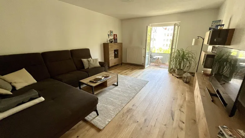 Helles Wohnzimmer mit Holzboden, gemütlichem Sofa und direktem Zugang zum Balkon.