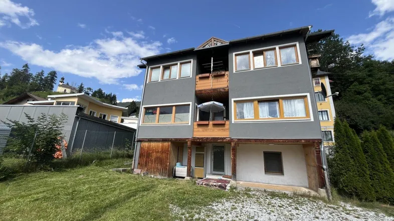 Mehrfamilienhaus mit mehreren Balkonen und Terrassen in einer grünen Umgebung.