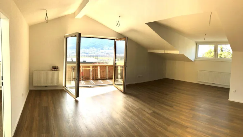 Helles Dachgeschoss-Wohnzimmer mit Holzboden und Zugang zu einem Balkon mit Bergblick.