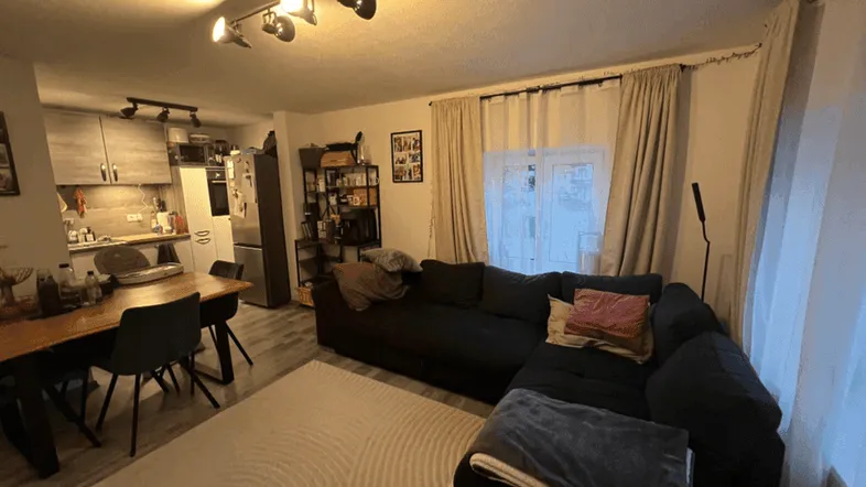 Gemütlicher offener Wohn- und Essbereich mit dunklem Sofa, Esstisch und integrierter Küche.