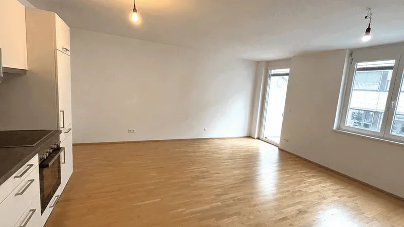 Helles Wohnzimmer mit integrierter Küche und Zugang zum Balkon, ausgestattet mit Parkettboden.