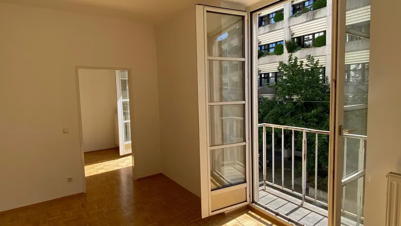 Helles Wohnzimmer mit Parkettboden, Zugang zum Balkon und Blick auf die Stadt.