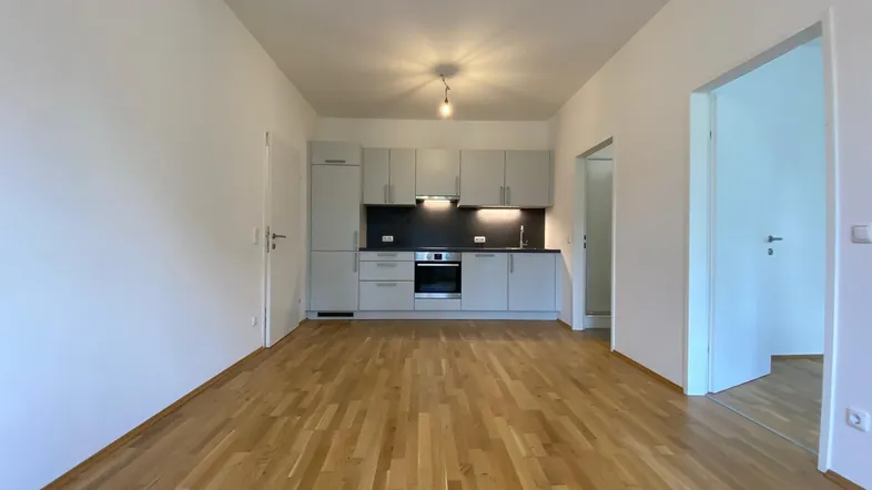 Moderne offene Küche in hellem Raum mit Holzparkettboden und grauen Schränken, bereit zur Nutzung.