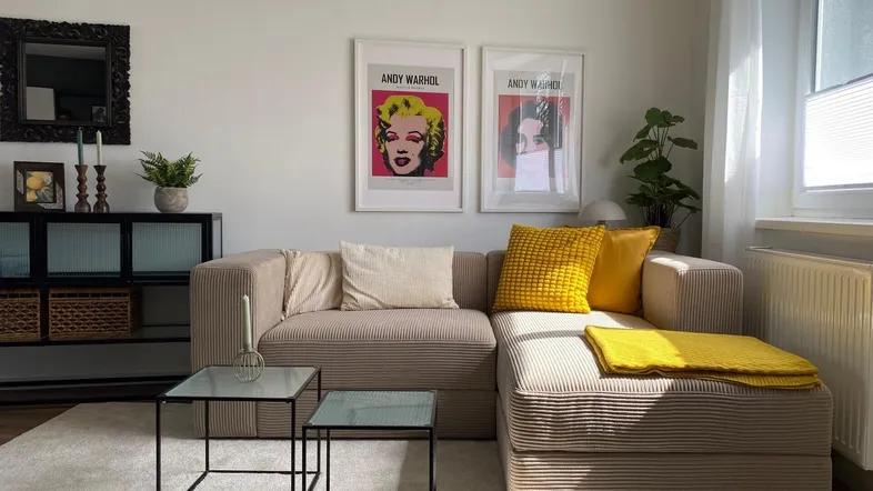 Helles Wohnzimmer mit beigem Ecksofa, modernen Beistelltischen und Kunstwerken an der Wand.