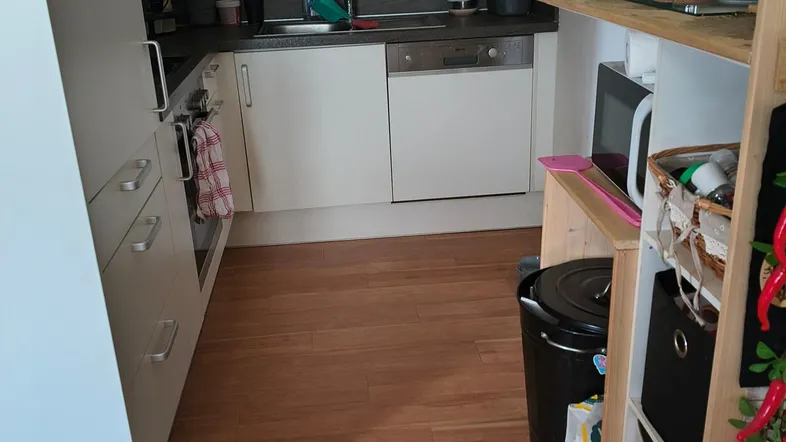Moderne Küche mit weißen Schränken, dunkler Arbeitsplatte, Geschirrspüler und Holzboden.