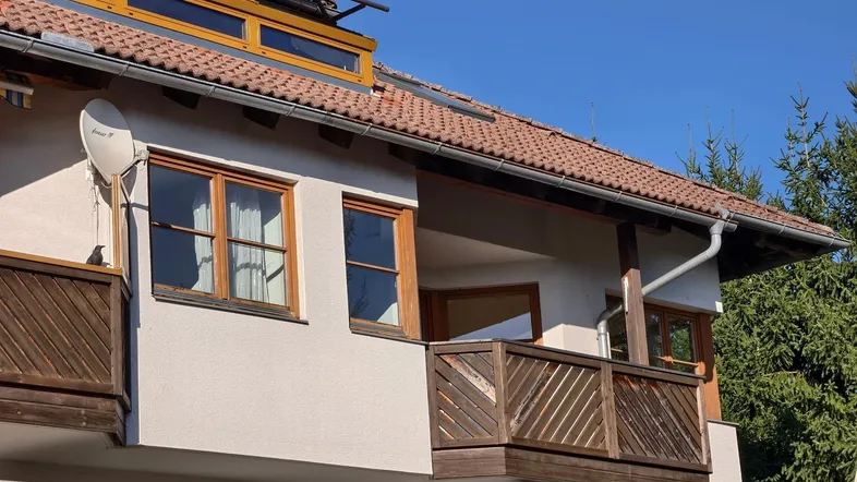 Fassade eines Wohngebäudes mit Holzbalkonen und einem Ziegeldach unter blauem Himmel.