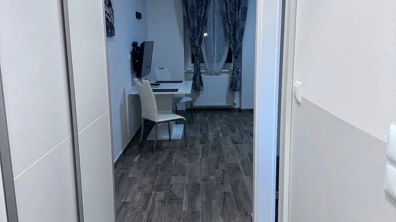 Langer, schmaler Flur mit Holzoptikboden, der zu einem Arbeitsbereich führt.