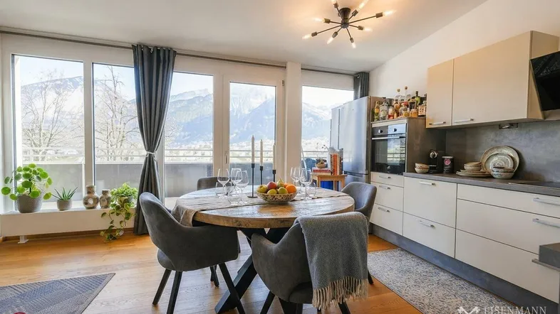 Heller Wohn- und Essbereich mit Holzboden, moderner Küche und beeindruckendem Bergblick.