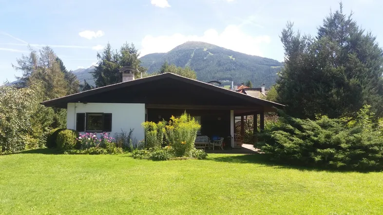 Charmantes Haus mit großem Garten und überdachter Terrasse, umgeben von grüner Natur und Bergblick.