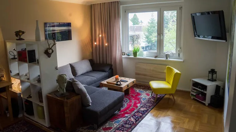 Gemütliches Wohnzimmer mit Sofa, gelbem Sessel, Parkettboden und Blick ins Grüne.