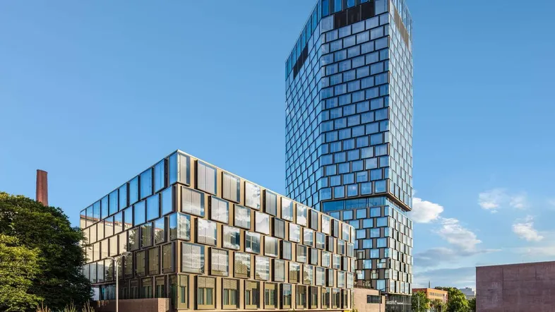 Modernes Hochhaus und angrenzendes Gebäude mit Glasfassaden unter blauem Himmel.