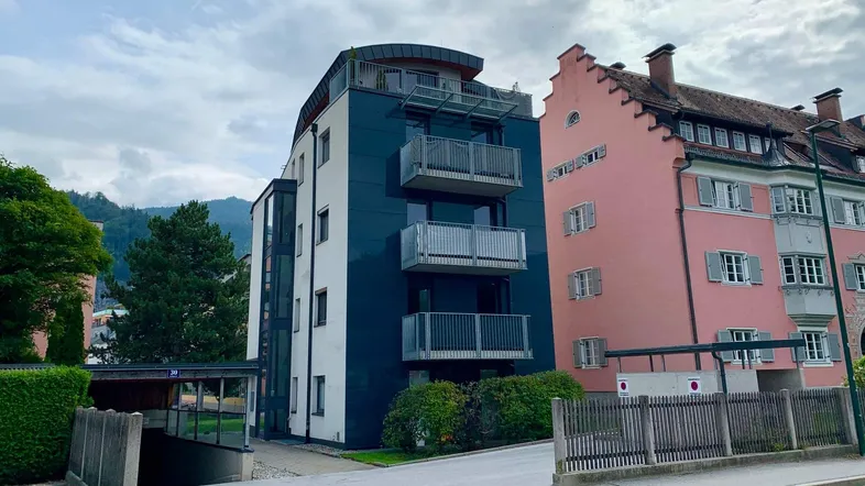 Modernes Mehrfamilienhaus mit Balkonen und Tiefgaragenzufahrt neben einem historischen Gebäude.