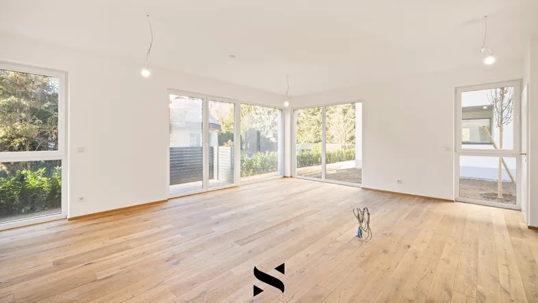 Helles und geräumiges Wohnzimmer mit großen Fenstern, Holzboden und Zugang zum Garten.
