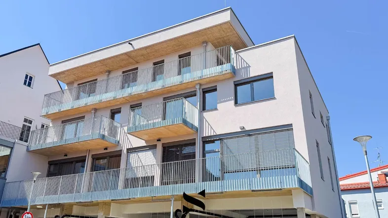 Moderne Gebäudefassade mit mehreren Balkonen und großen Fenstern unter blauem Himmel.