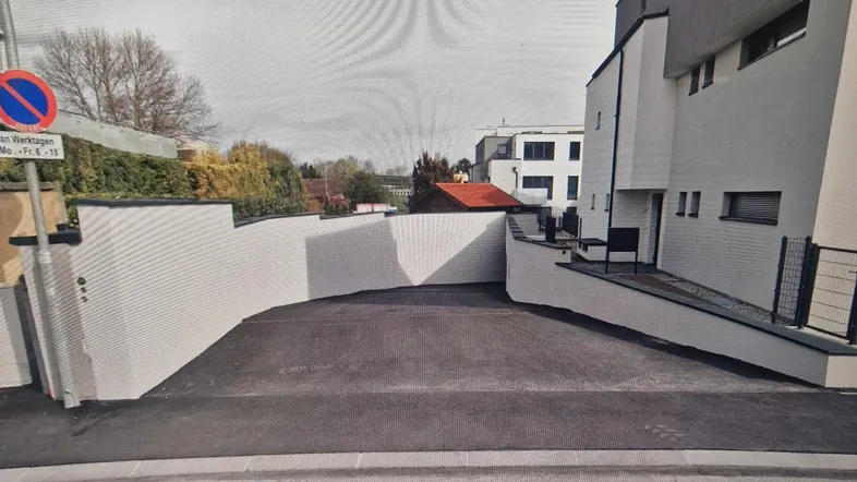 Moderne Gebäudeansicht mit Zufahrt zu einem Parkbereich und weißer Fassade unter hellem Himmel.