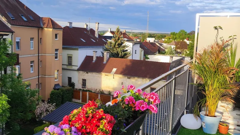Heller Balkon mit Kunstrasen, bunten Blumen und weitem Blick über die Stadt.