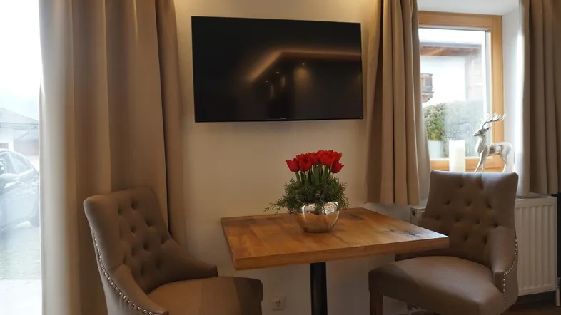 Gemütlicher Sitzbereich mit Fernseher, Holztisch und Blick nach draußen durch das Fenster.