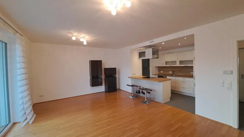 Heller offener Wohn- und Essbereich mit integrierter Küche, Parkettboden und Zugang zum Balkon.