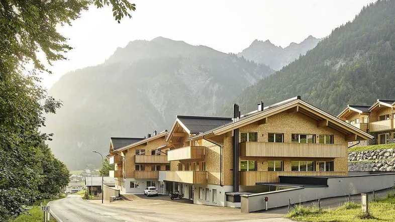 Moderne Holzfassaden der Gebäude in alpiner Landschaft mit Bergblick und Zufahrtsstraße.