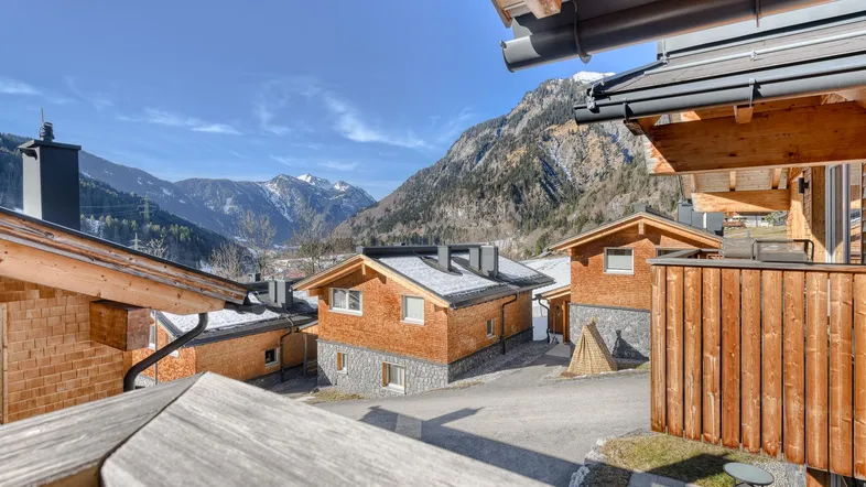 Blick auf charmante Holzchalets mit verschneiten Dächern und majestätischer Bergkulisse unter blauem Himmel.