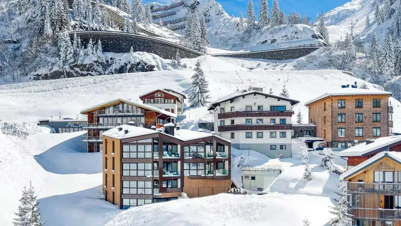 Mehrere moderne Gebäude in einer verschneiten Berglandschaft unter blauem Himmel.