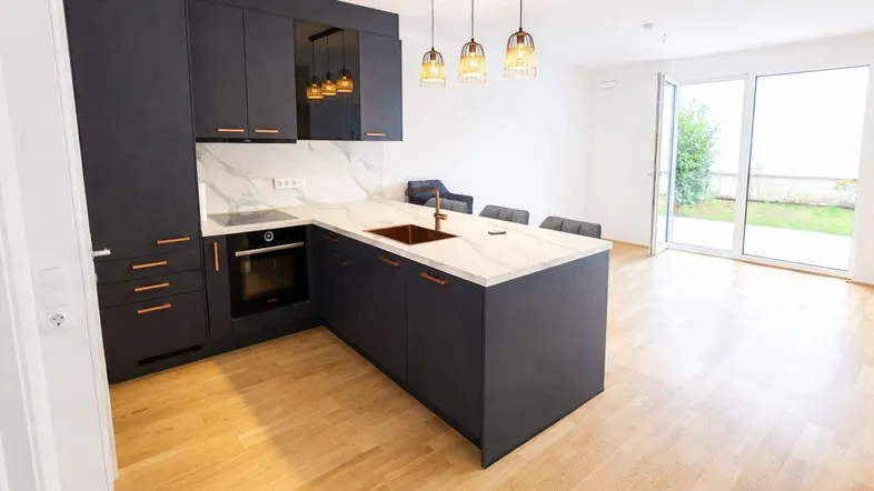 Moderne Küche mit dunklen Schränken, heller Arbeitsplatte und Zugang zum Gartenbereich.