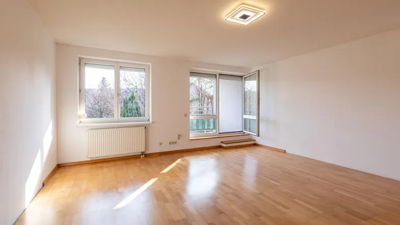 Helles, unmöbliertes Zimmer mit Parkettboden und Zugang zum Balkon, gut belichtet durch große Fenster.