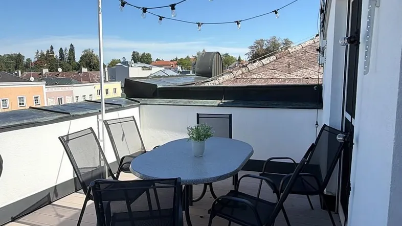 Sonnige Dachterrasse mit Holzboden, Gartenmöbeln und Blick über die Dächer der Stadt.