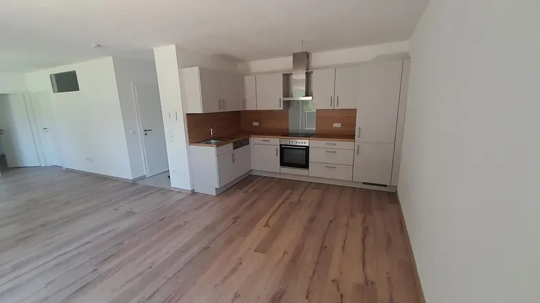 Heller offener Wohnbereich mit integrierter Küche, modernem Laminatboden und viel Tageslicht.