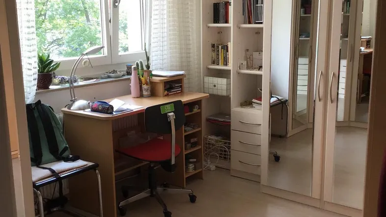 Helles Schlafzimmer mit Schreibtisch, großem Fenster und integriertem Spiegelschrank, bietet einen grünen Ausblick.